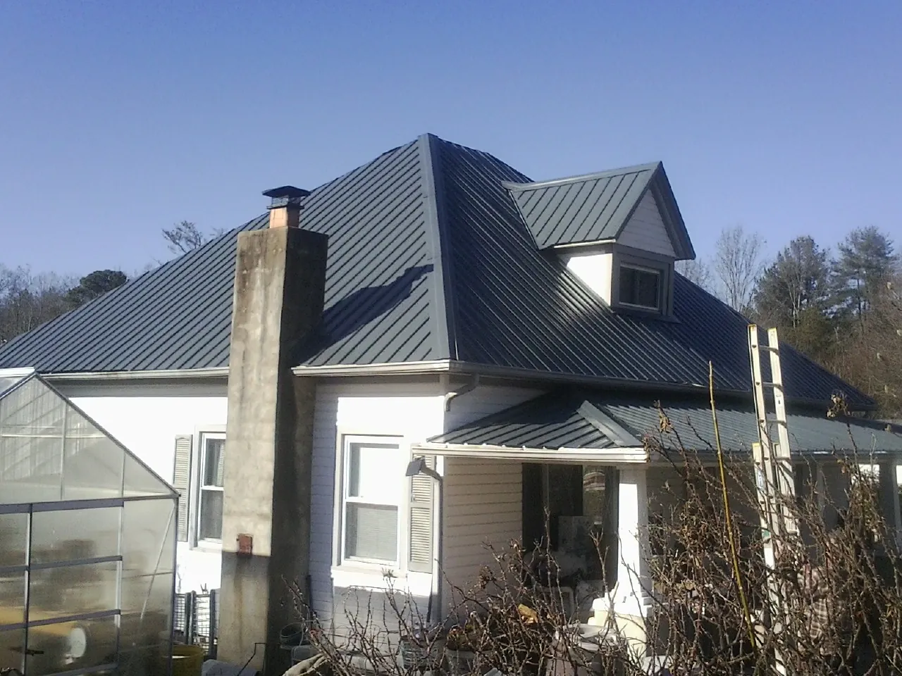 Dark blue standing seam metal roof on a white farmhouse with dormer — Slate & Tile Roof Repair by Roofing Brothers in Edison
