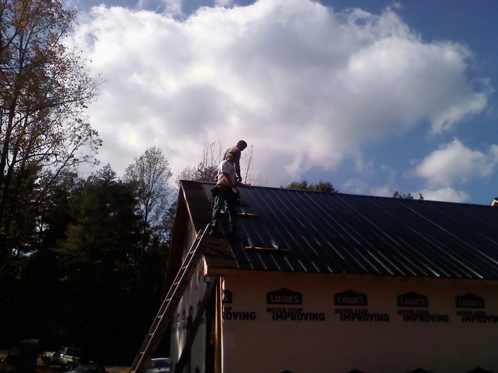 Roofer fastening dark metal panels high against a cloudy sky, from a Roof Inspection job in Edison