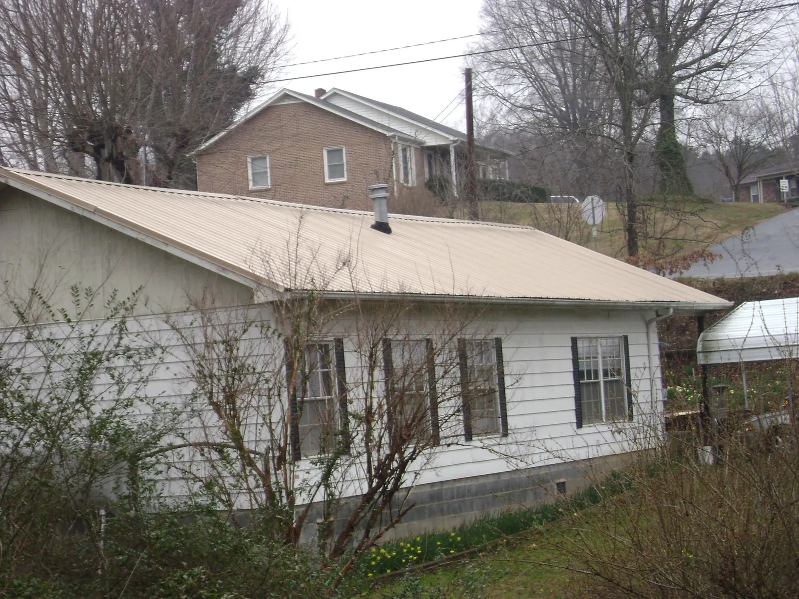 Tan metal roof on a white sided house set into a hillside — Commercial Roofing by Roofing Brothers in Edison